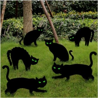 Silhouettes of black cats with green eyes in a garden.